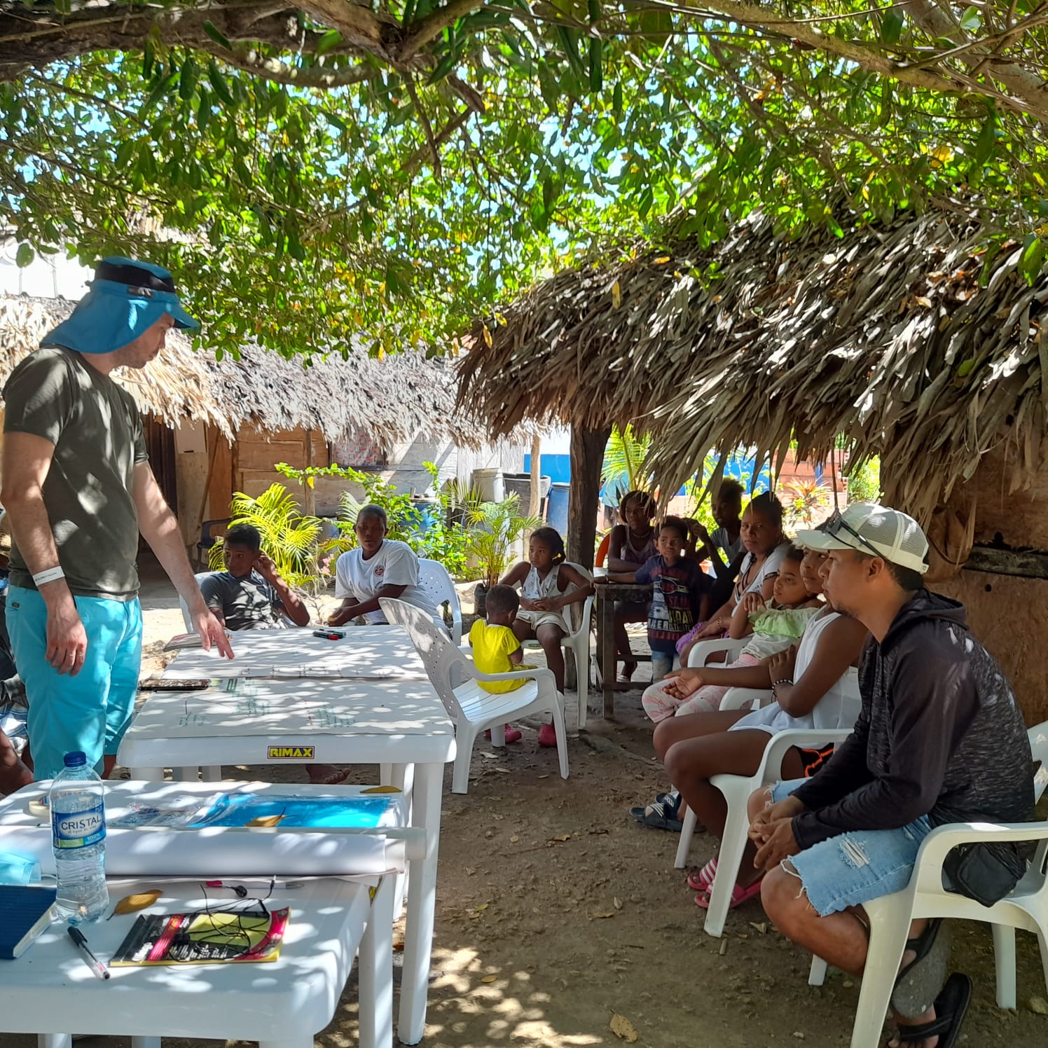 Trainer teaching a coastal community seated under a thatched roof